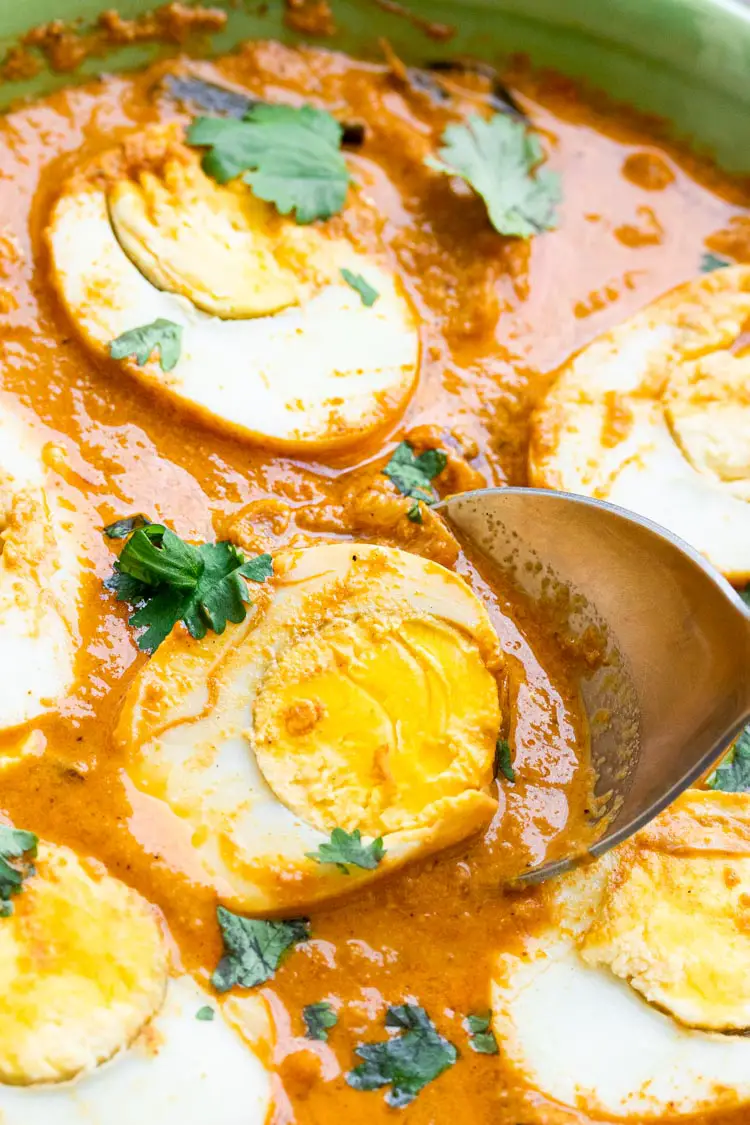 close up shot of egg curry with a spoon scooping out an egg