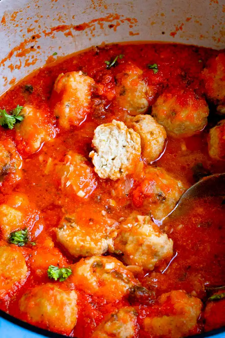 a ladle inside a cast iron dutch oven full of chicken meatballs and spaghetti sauce, a ladle inside a cast iron dutch oven full of chicken meatballs and spaghetti sauce