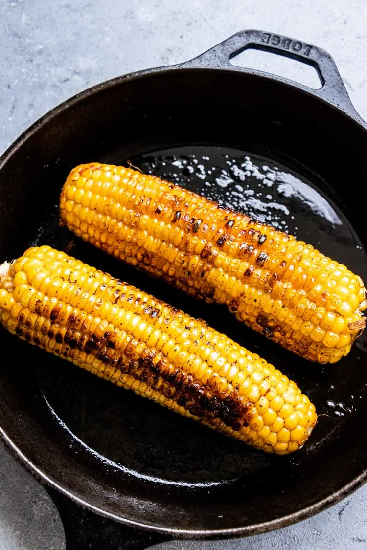 Two corn cobs roasted or grilled on a cast iron skillet